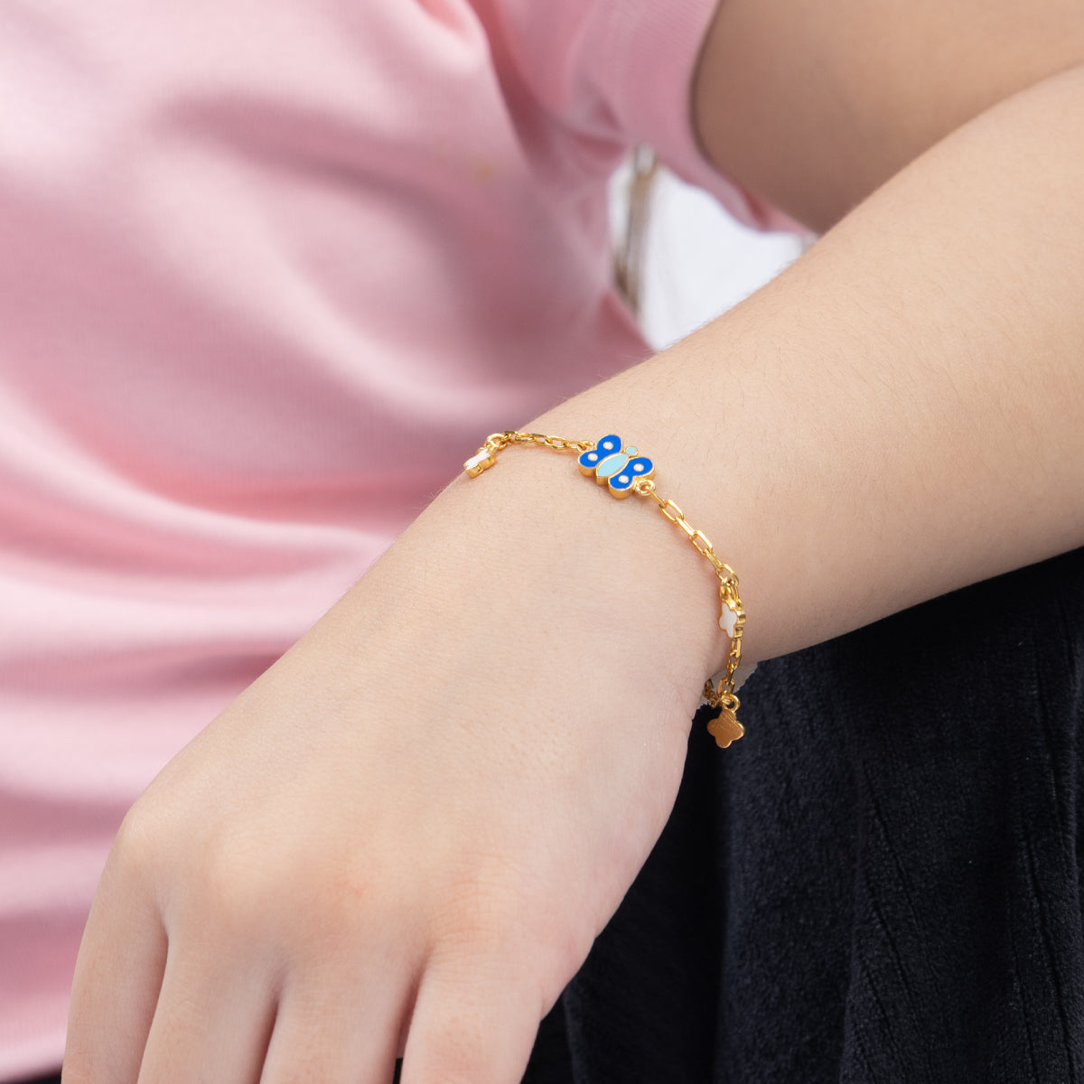 Tiny Jewels gold bracelet with blue accents on a wrist against a pink and black background