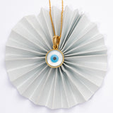 Tiny Jewels necklace with a circular pendant featuring an eye design on a white background