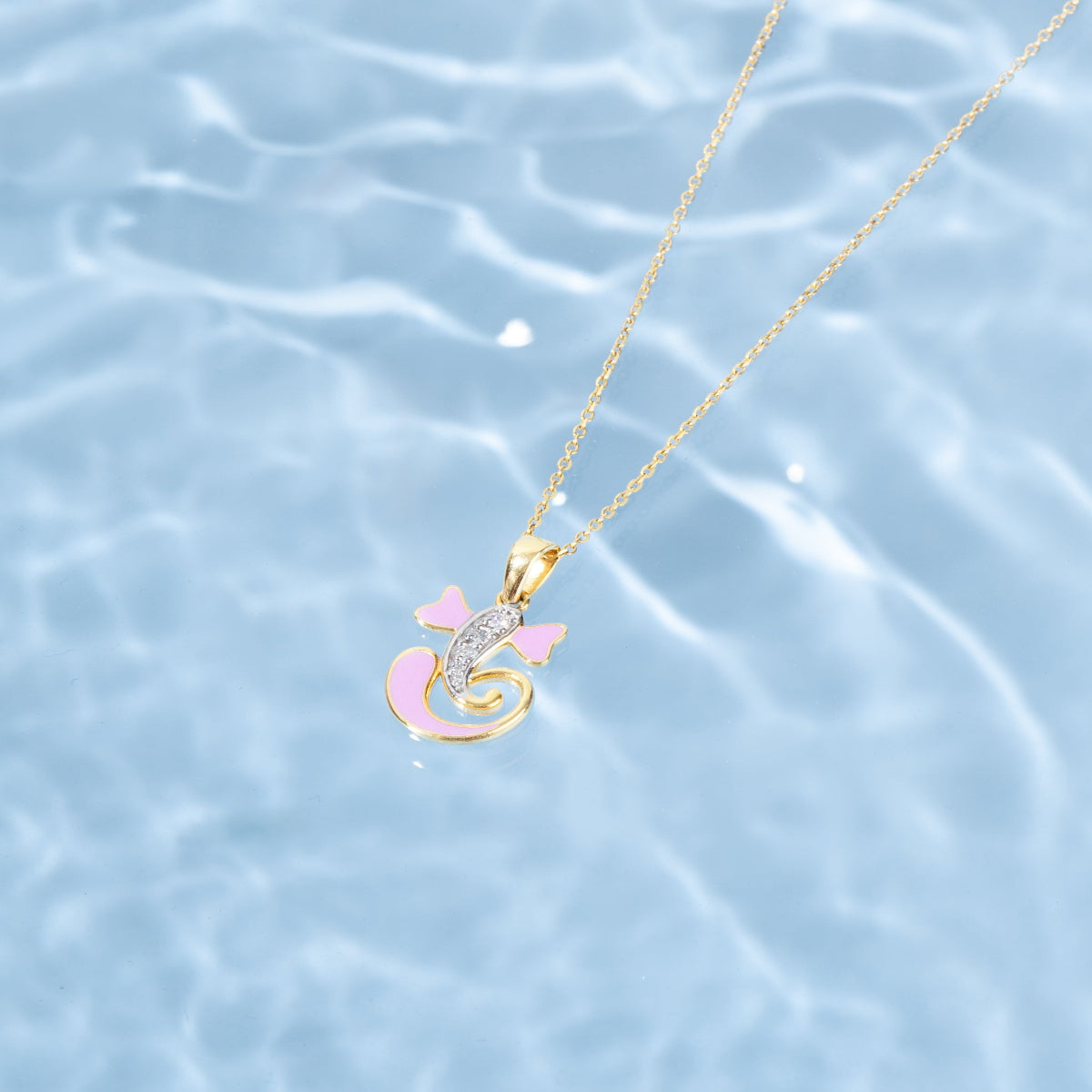 Gold necklace with a pink pendant on a water background  Tiny Jewels.