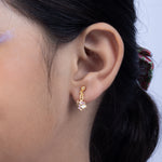 Tiny Jewels close-up of an ear wearing a gold earring with a pink gemstone.