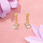 Tiny Jewels gold earrings with heart and flower charms on a pink floral background