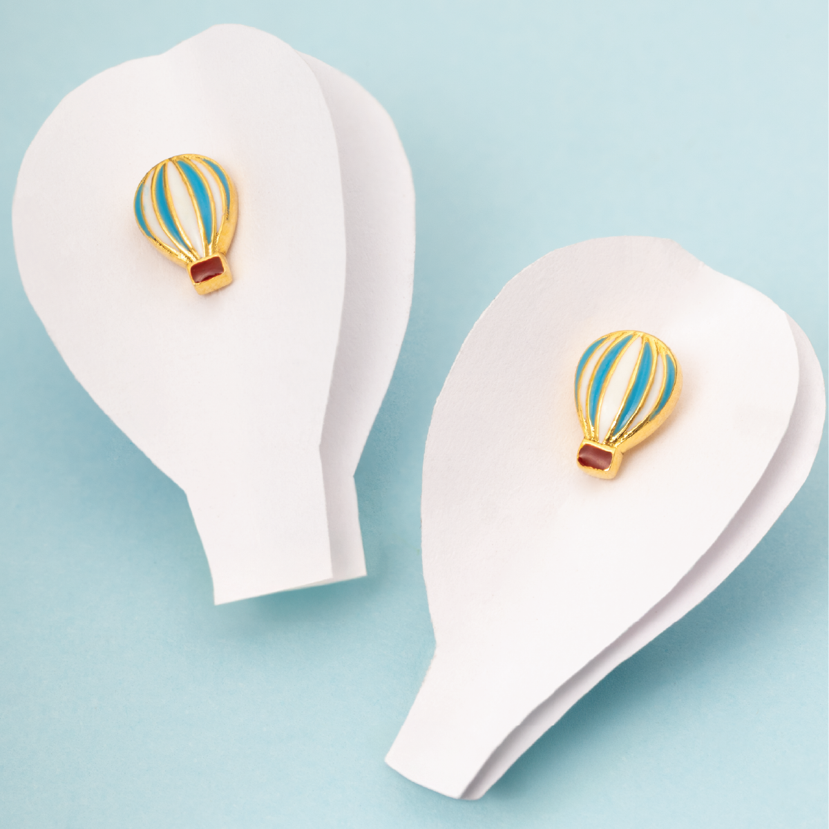 Tiny Jewels hot air balloon earrings on white earring stands against a light blue background