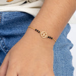 Tiny Jewels gold bracelet with black beads on a wrist against a denim background