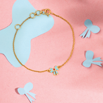 Tiny Jewels gold bracelet with a blue butterfly charm on a pink background