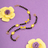 Tiny Jewels necklace with black beads and yellow butterfly pendants on a purple background with yellow flowers.