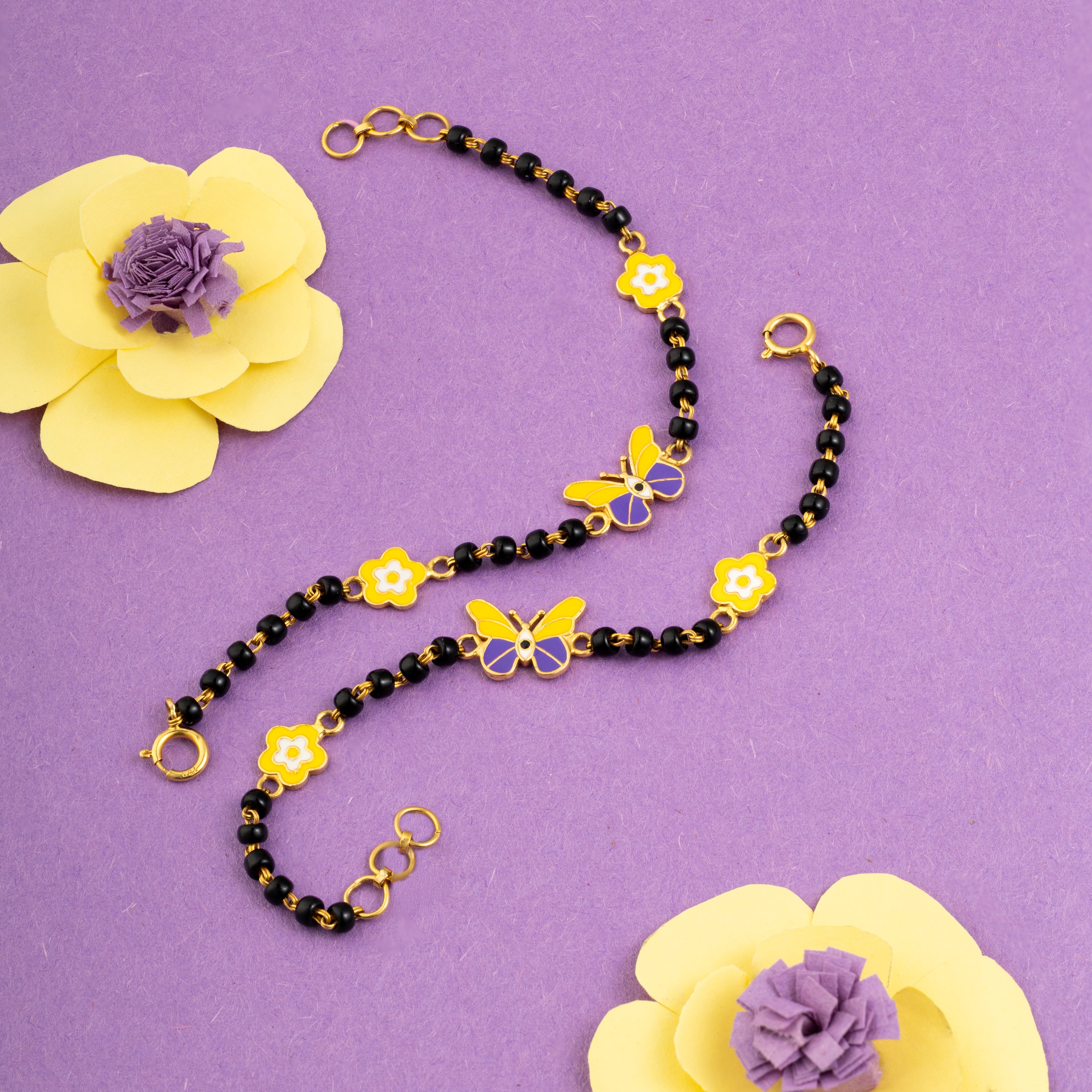 Tiny Jewels necklace with black beads and yellow butterfly pendants on a purple background with yellow flowers.