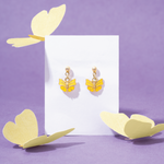 Tiny Jewels yellow butterfly earrings on a white card with decorative yellow leaves on a purple background