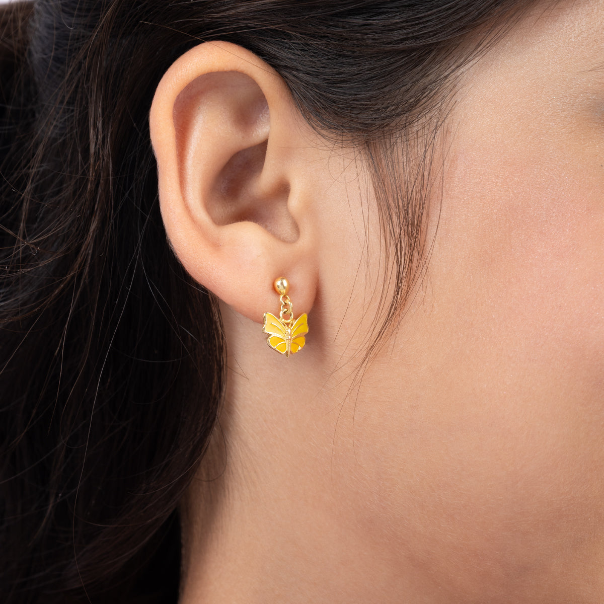 Tiny Jewels close-up of an ear wearing a yellow flower-shaped earring with dark hair.