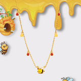 Tiny Jewels gold necklace with bee charms on a background with honey and bees