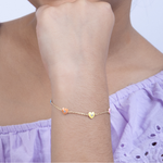 Tiny Jewels gold bracelet with heart charm on a wrist, wearing a light purple top.