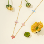 Tiny Jewels necklace with floral pendants on a light background with flowers