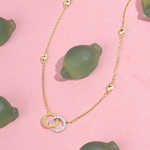 Tiny Jewels gold necklace with circular pendant on a pink background with green lemons