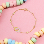 Tiny Jewels gold bracelet with interlocking rings on a pink background with colorful beads.