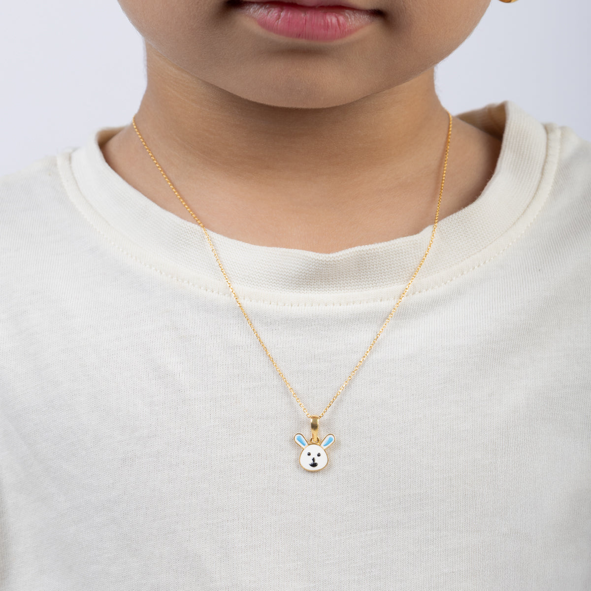 Tiny Jewels Child wearing a gold necklace with a bunny pendant on a plain background