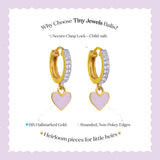 Tiny Jewels gold hoop earrings with heart charms on a light purple background, featuring text about product features.