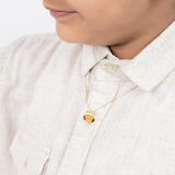 Tiny Jewels child wearing a gold necklace with a small pendant on a white shirt