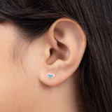 Tiny Jewels close-up of an ear wearing a heart-shaped earring with a blue center.