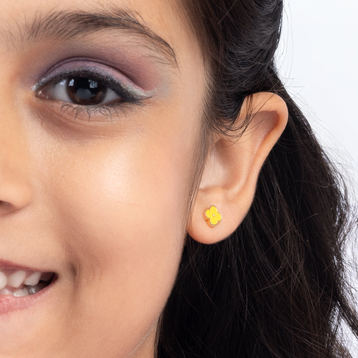 Tiny Jewels close-up of a woman wearing a yellow flower-shaped earring on a white background