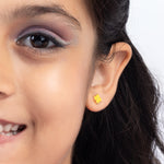 Tiny Jewels close-up of a woman wearing a yellow flower-shaped earring on a white background
