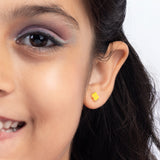Tiny Jewels close-up of a woman wearing a yellow flower-shaped earring on a white background