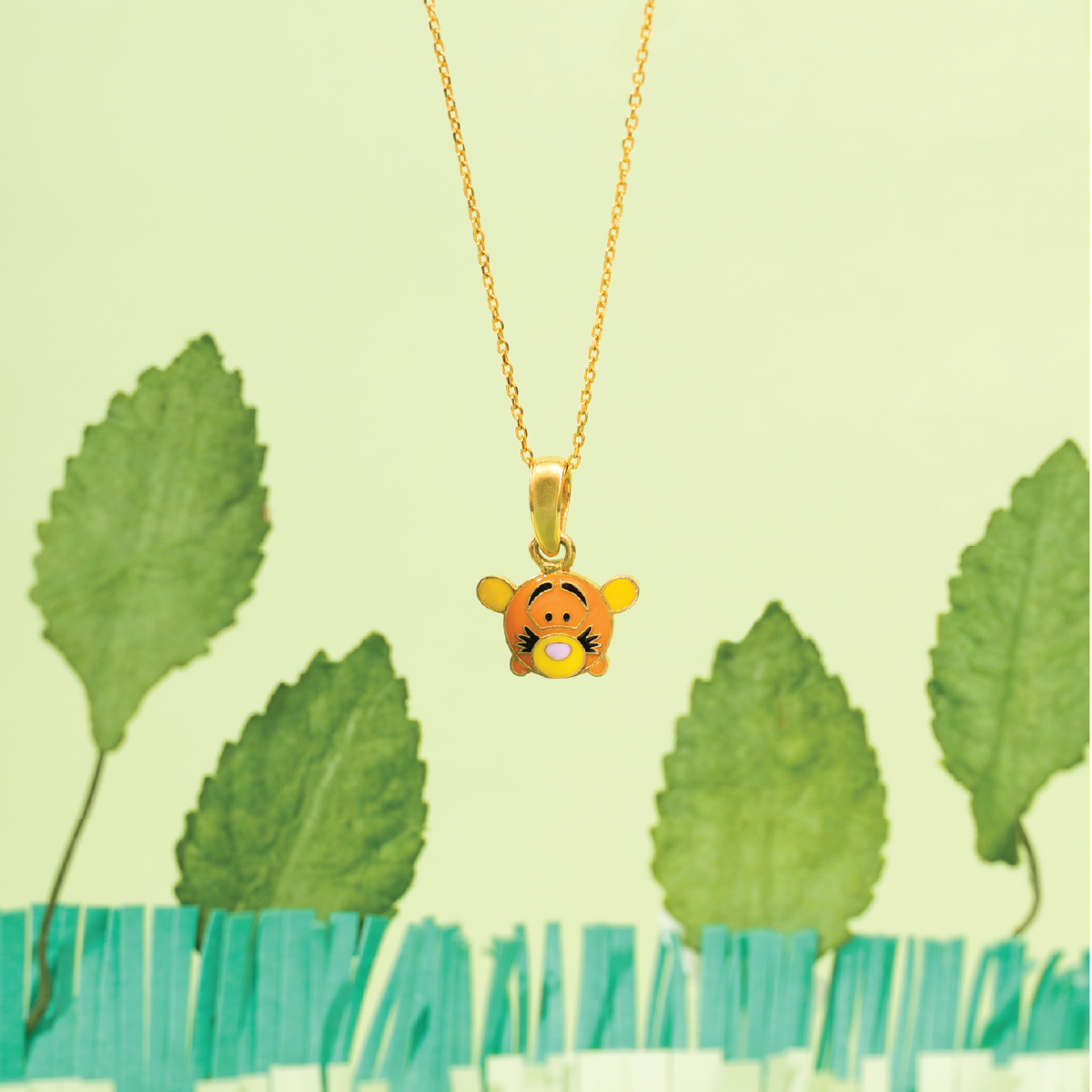 Tiny Jewels gold necklace with a cartoon character pendant against a green leafy background