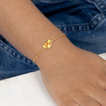 Tiny Jewels gold bracelet with a floral charm on a wrist against a blue denim background