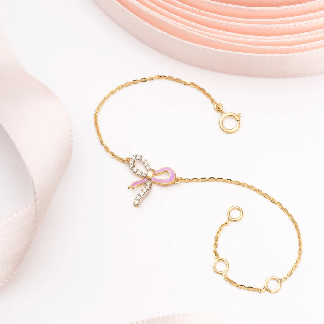 Tiny Jewels gold bracelet with a decorative bow charm on a light background