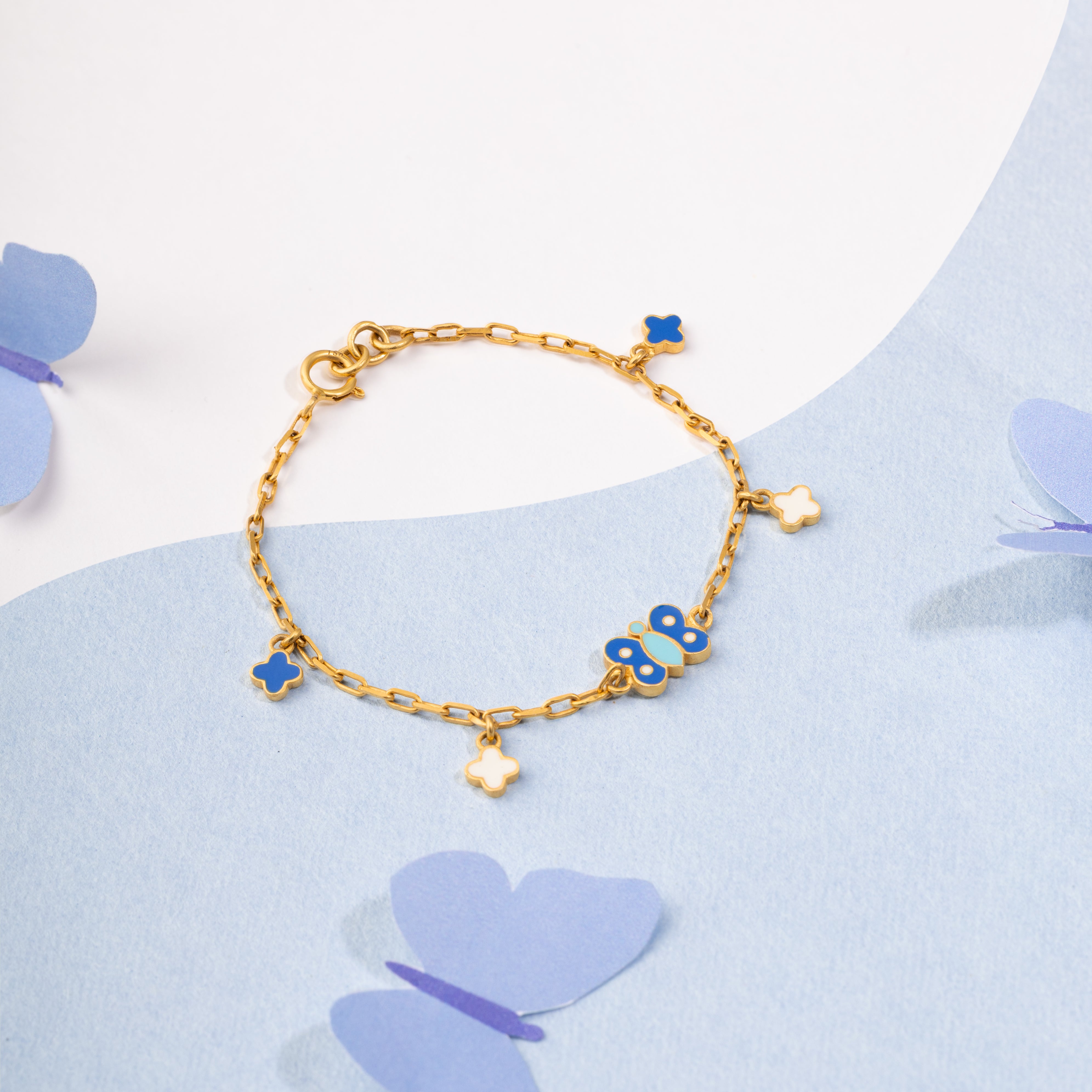Tiny Jewels gold bracelet with blue charms on a light blue background