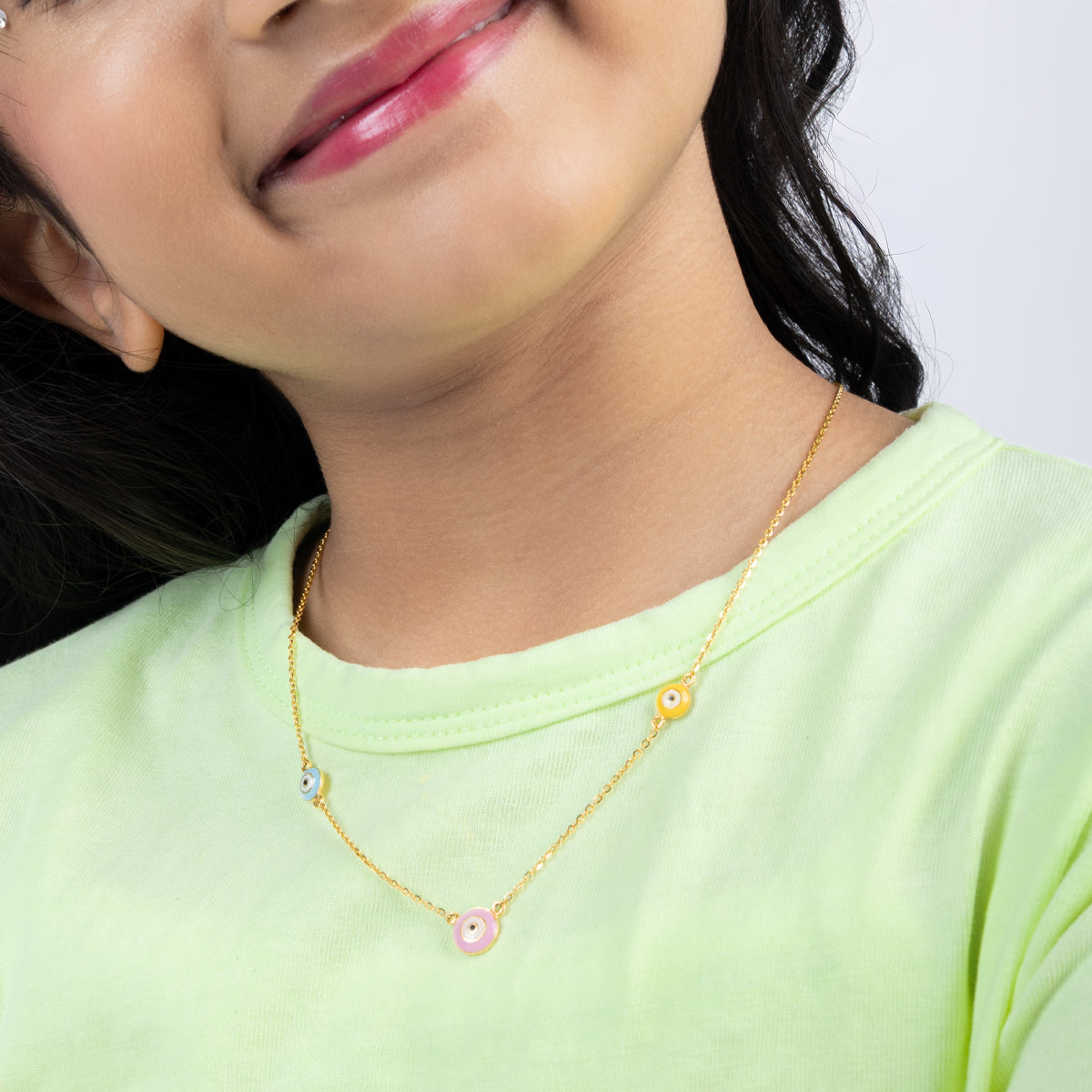 Tiny Jewels close-up of a person wearing a gold necklace with colorful beads on a plain background