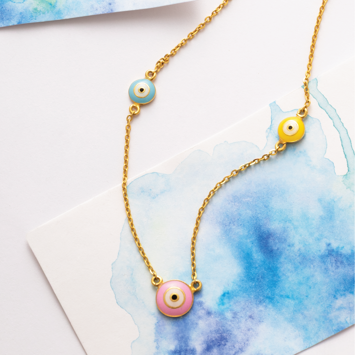 Tiny Jewels necklace with colorful evil eye charms on a watercolor background