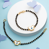 Tiny Jewels black beaded bracelet with gold butterfly charms on a white plate against a blue background