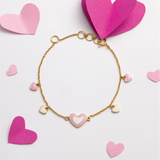 Tiny Jewels gold bracelet with heart charms on a light pink background with pink hearts