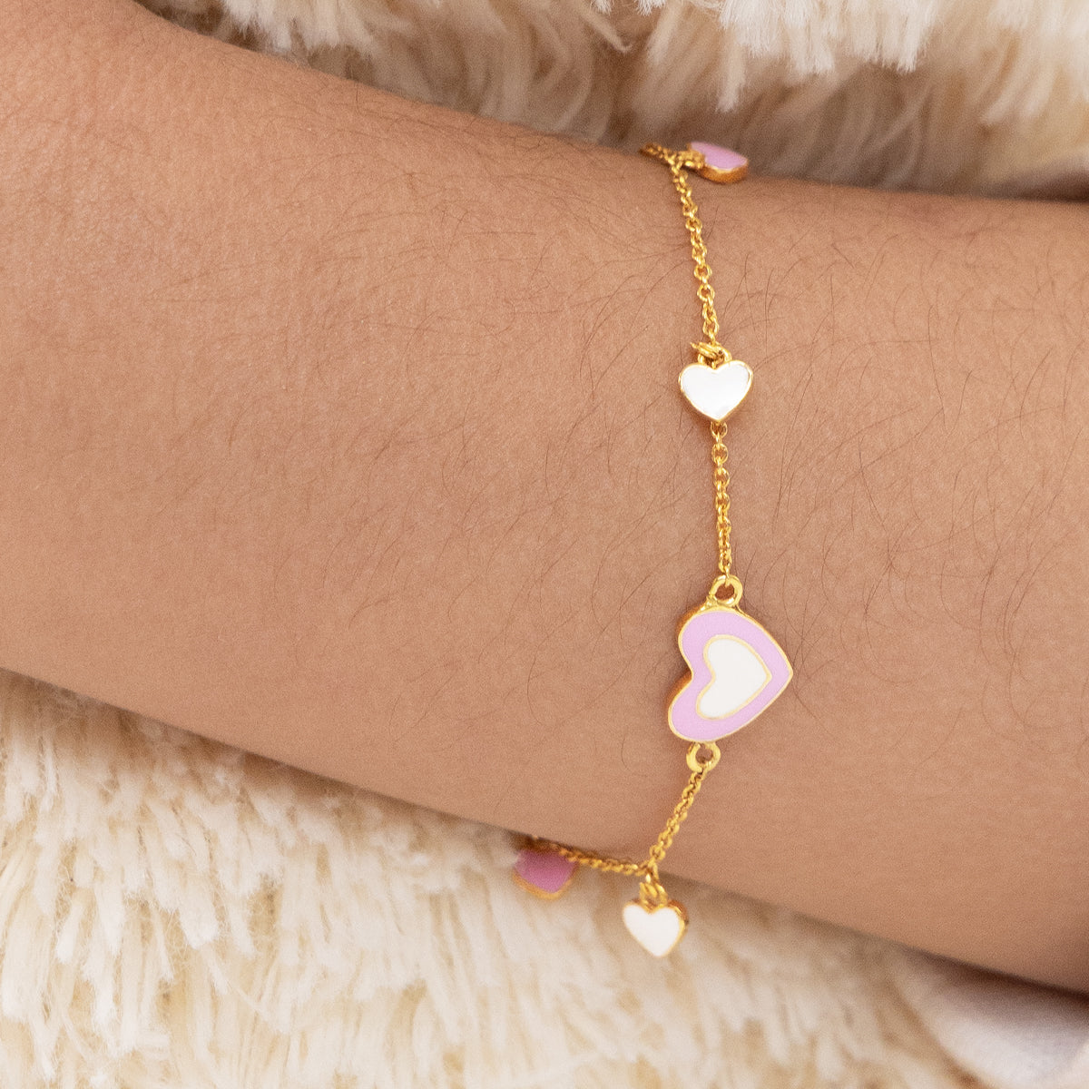 Tiny Jewels gold bracelet with heart-shaped charms on a wrist against a soft background