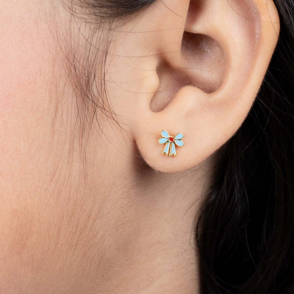 Tiny Jewels close-up of an ear wearing a small blue and gold earring.