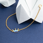 Tiny Jewels gold bracelet with a blue crown charm on a blue background