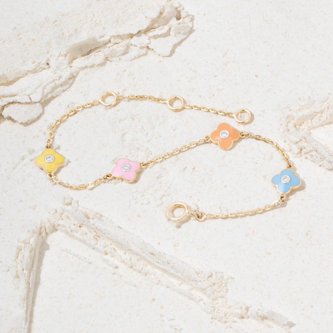 Tiny Jewels gold bracelet with colorful flower-shaped charms on a marble surface