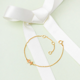 Tiny Jewels gold bracelet on a white ribbon with a light green background