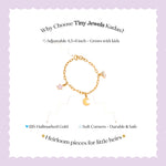 Tiny Jewels gold bracelet with charms on a light purple background, featuring text about Tiny Jewels Kadas.