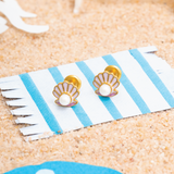 Tiny Jewels shell-shaped earrings on a striped card with sand background