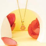 Tiny Jewels gold necklace with a pink flower pendant on a yellow and red floral background