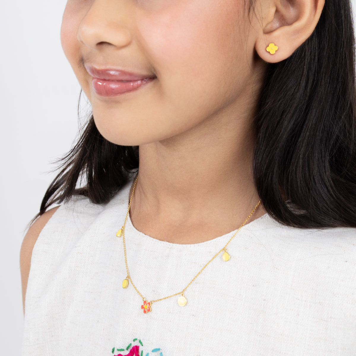 Tiny Jewels close-up of a person wearing a gold necklace and earrings on a white background