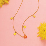 Tiny Jewels necklace with yellow pendants on a pink background with yellow flowers