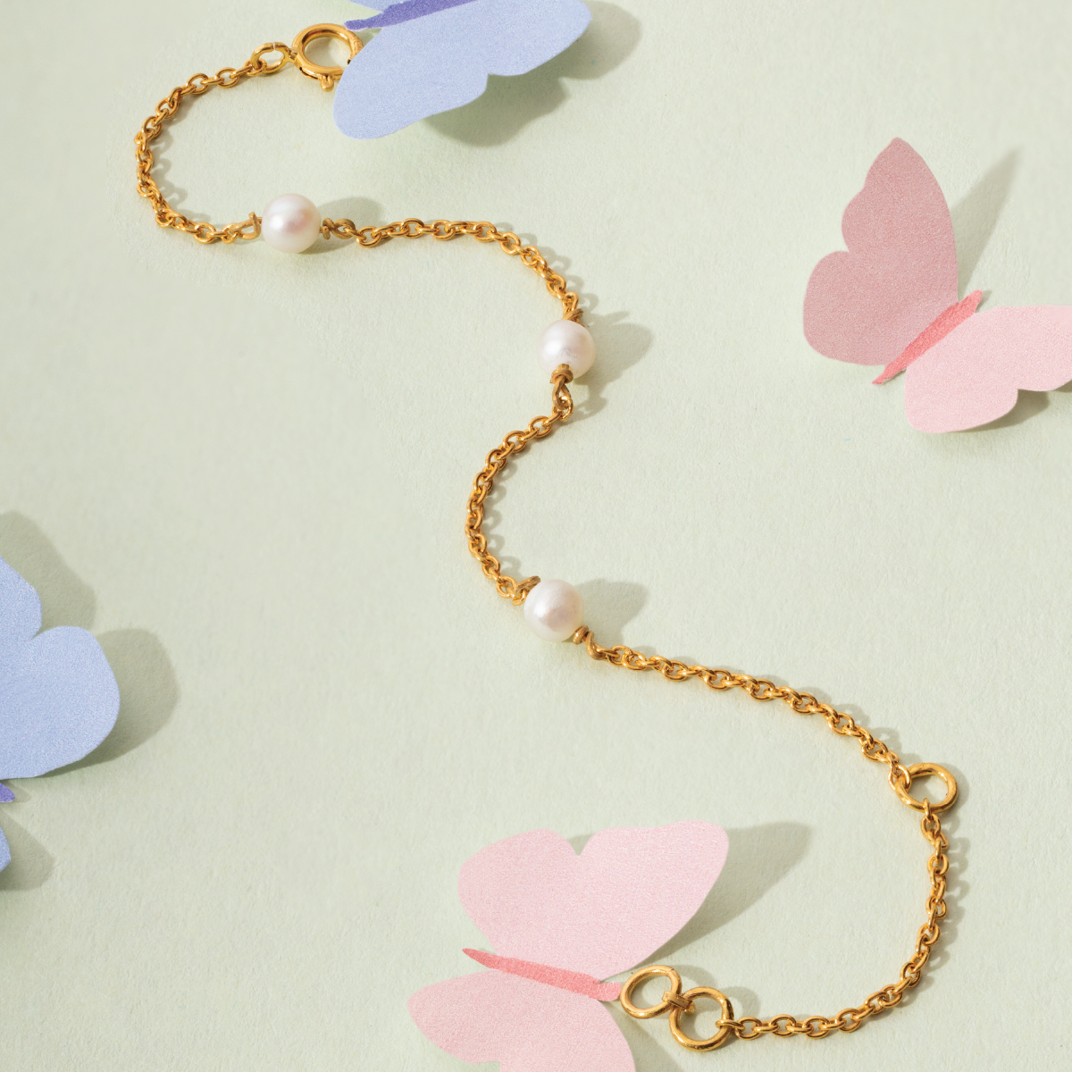Tiny Jewels gold chain necklace with pearls on a light green background with butterfly decorations