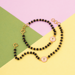Tiny Jewels necklace with black beads and gold accents on a colorful geometric background
