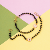 Tiny Jewels necklace with black beads and gold accents on a colorful geometric background