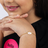 Tiny Jewels close-up of a person wearing a gold bracelet with a pink stone on a plain background