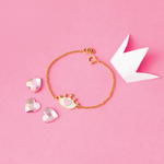 Tiny Jewels gold bracelet with heart-shaped charms on a pink background
