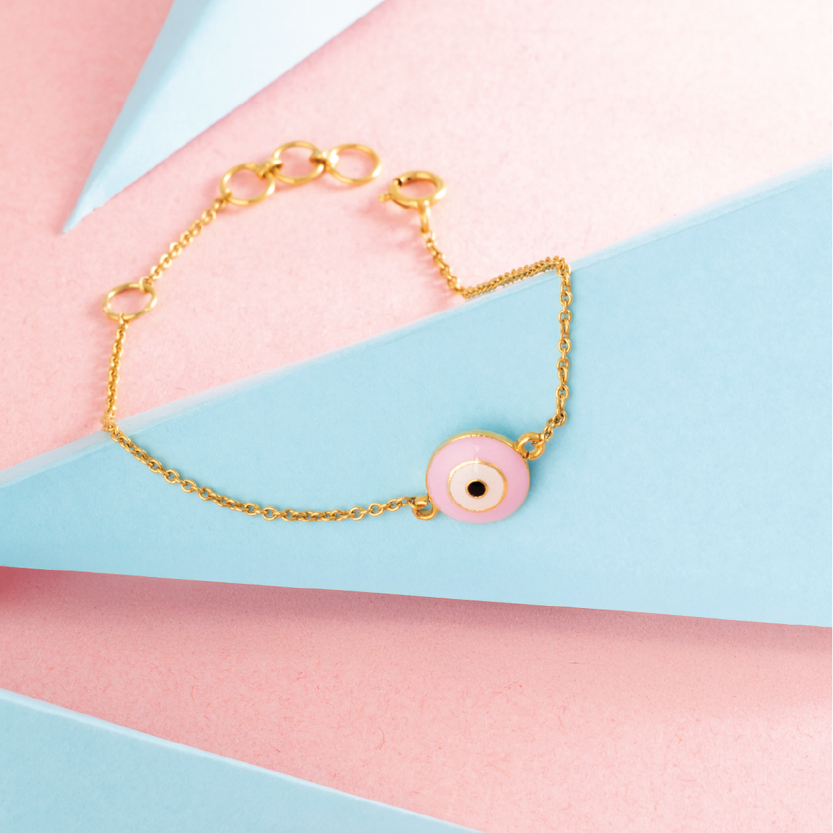 Tiny Jewels gold bracelet with a pink evil eye charm on a colorful background