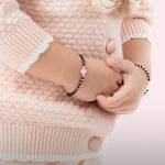 Tiny Jewels person wearing a pink heart bracelet on a light pink sweater background