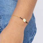 Tiny Jewels gold bracelet with black beads and a symbol worn on a wrist against a denim background